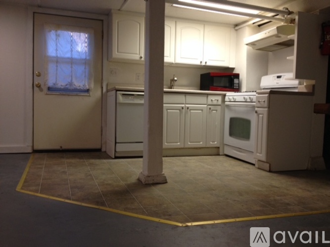 A kitchen with white cabinets and appliances, a window with curtains, and a yellow line on the floor.