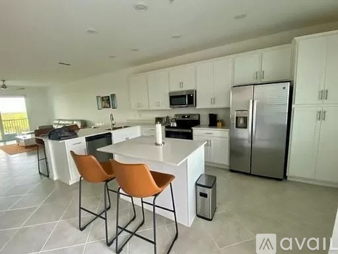 A kitchen with white cabinets and a central island with chairs.