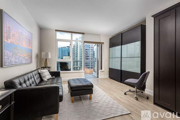 A living room with a black leather couch and ottoman, a grey rug, and a large window with a view of a city skyline.