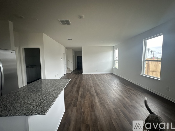 A cat is sitting on a wooden floor in a spacious room.