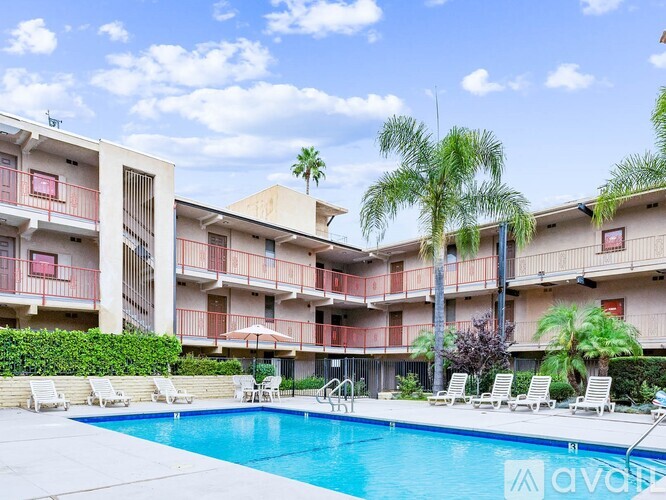 A swimming pool is surrounded by lounge chairs and palm trees in front of apartment buildings.