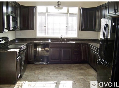 A kitchen with dark wood cabinets and a black refrigerator.