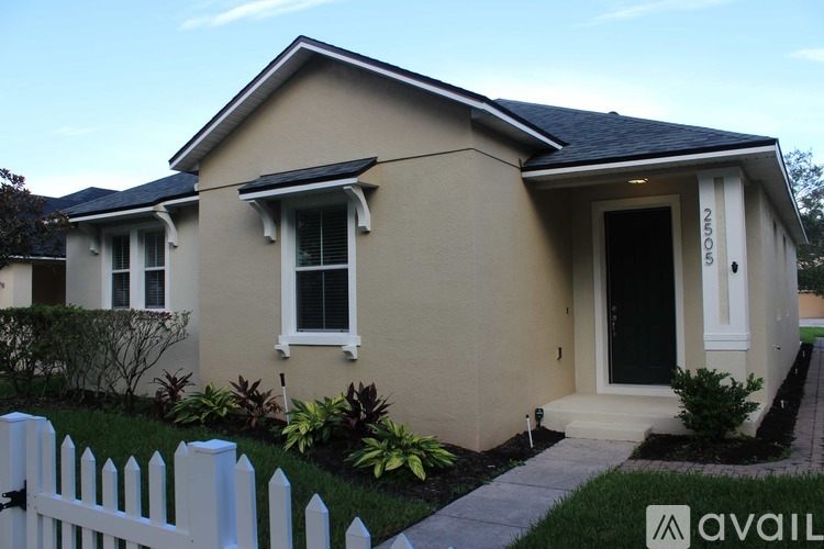 A beige house with a black door and a white picket fence.