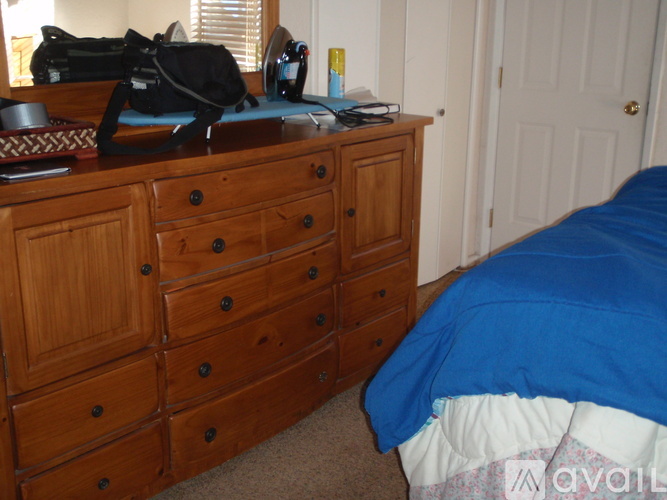 A blue bed sits next to a wooden dresser in a bedroom.