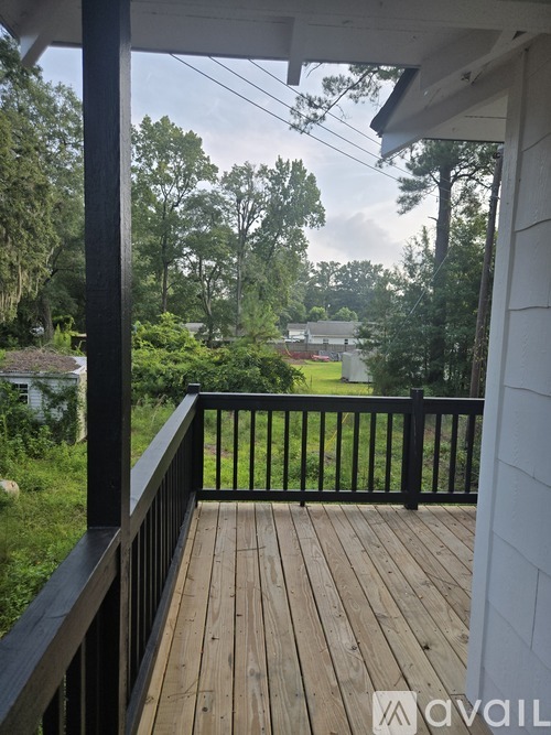 A wooden deck with a black railing and a view of a green lawn and trees.