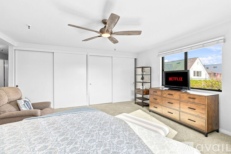 A bedroom with a bed, a couch, a dresser with a TV on top, and a ceiling fan.