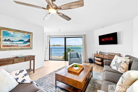 A living room with a ceiling fan, a couch, a coffee table, and a painting of a beach scene.