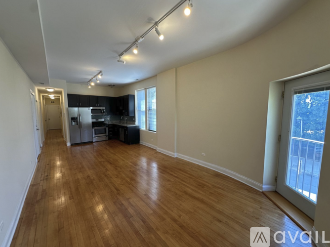A spacious room with wooden floors and a kitchen area in the background.