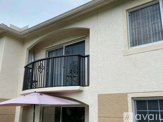 A balcony with a purple umbrella is attached to a beige building.