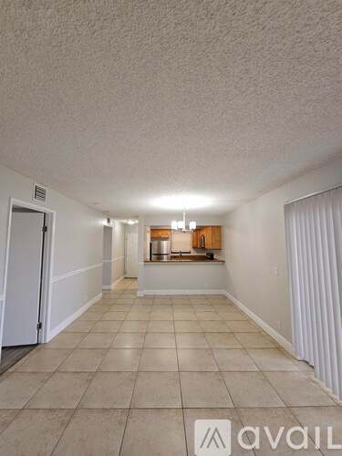 A spacious room with tiled flooring and a small kitchenette in the distance.