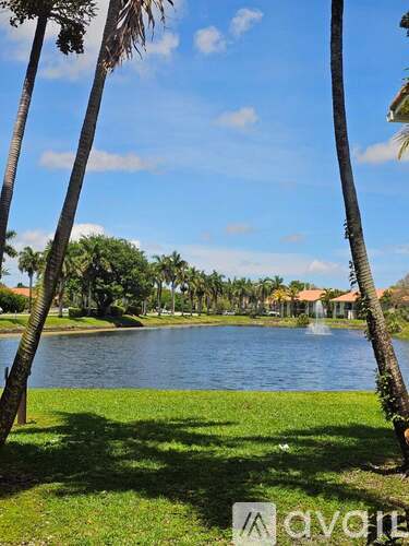A serene landscape with a lake, palm trees, and a clear sky.