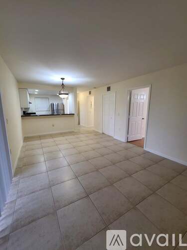 A spacious room with tiled flooring and a kitchen area in the background.