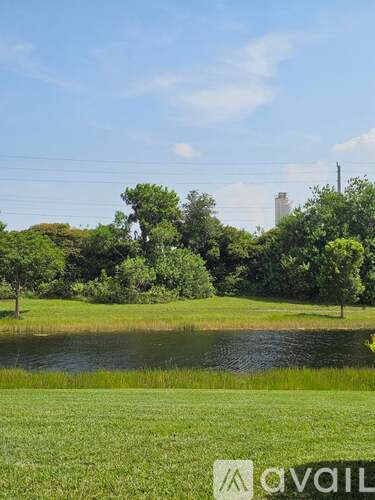 A grassy field with a pond and trees in the distance.