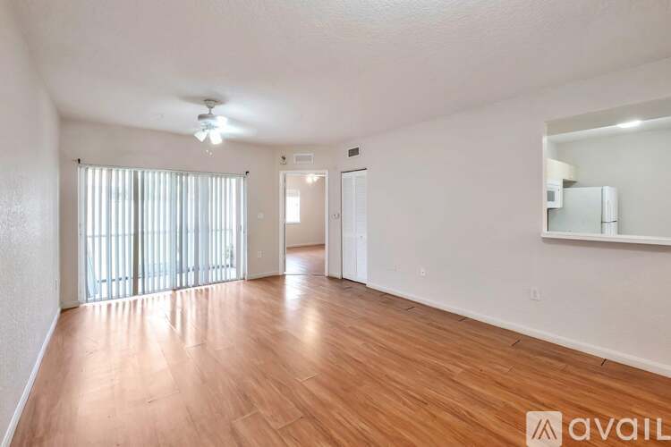 A spacious room with wooden flooring and a large window with blinds.