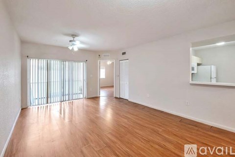 A spacious room with wooden flooring and a large window with blinds.