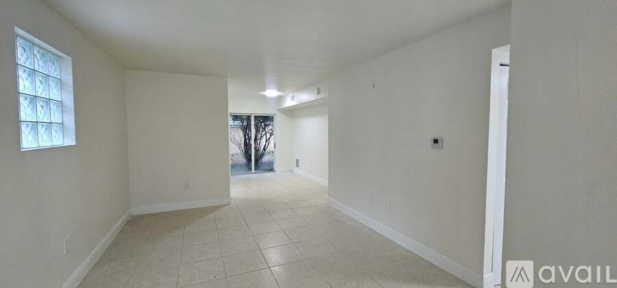 A spacious room with white walls and tiled flooring, featuring a window and a door leading to another room.