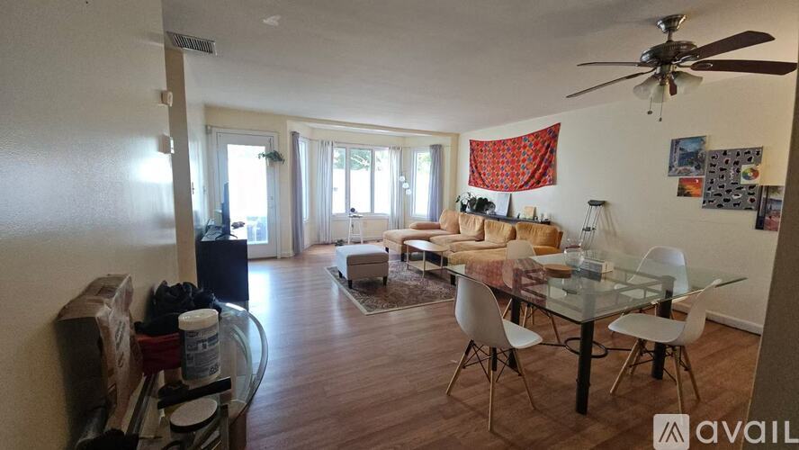 A living room with a glass table and chairs, a sofa, a ceiling fan, and a dining table with chairs.