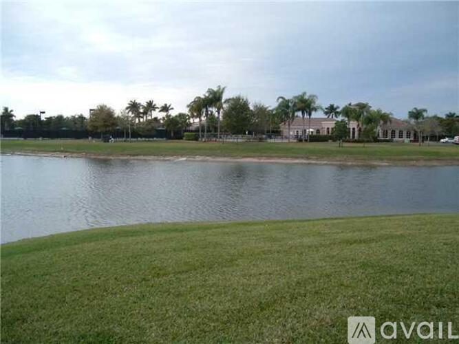 A grassy area in front of a body of water with buildings and trees in the background.