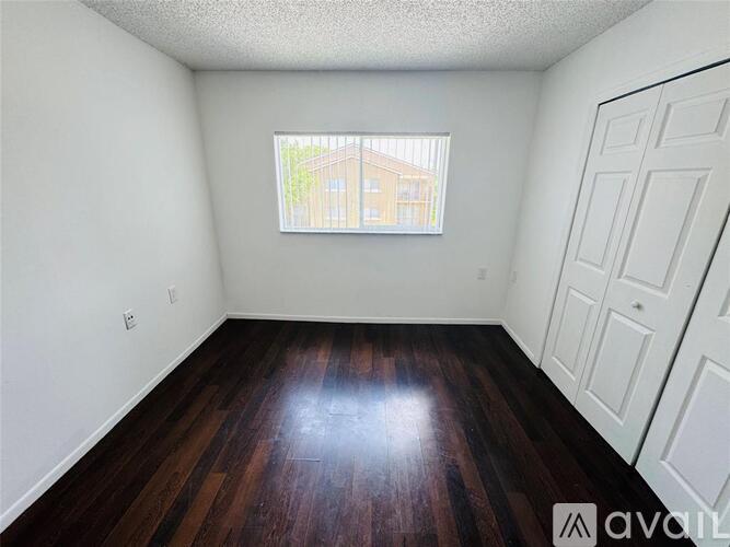 A room with wooden floors and white walls, with a window showing a building outside.