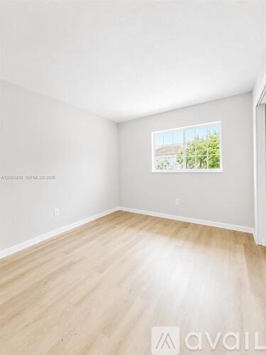 A room with wooden flooring and a window showing a view of a house and trees outside.
