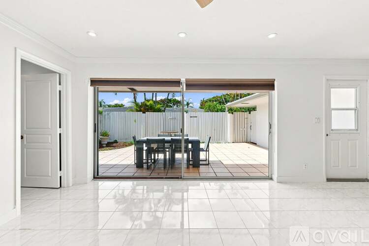 A dining room with a table and chairs is shown with a view of a backyard through a sliding glass door.