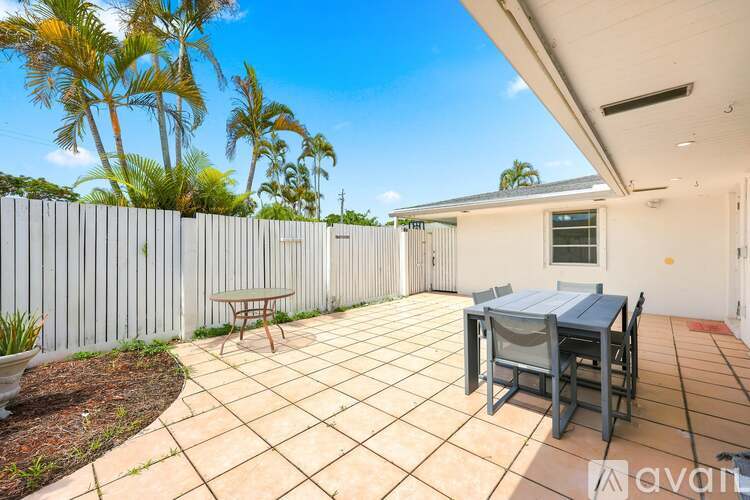 A patio with a table and chairs is surrounded by a white fence and palm trees.