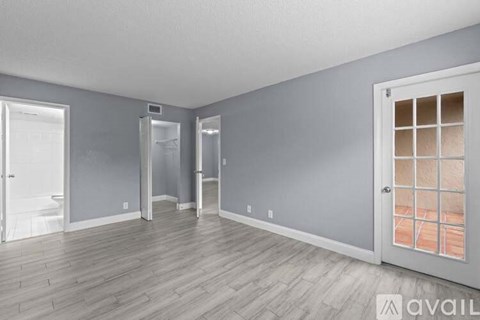 A room with grey walls and wooden flooring, with a door on the right side.