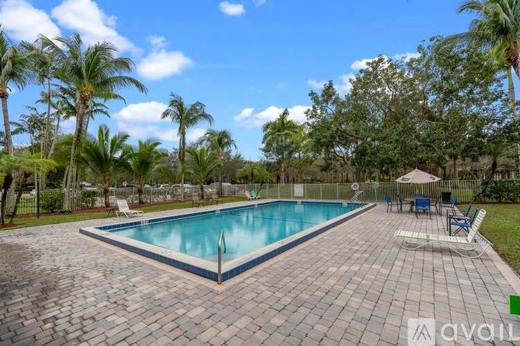 A pool surrounded by palm trees and a patio area with chairs.