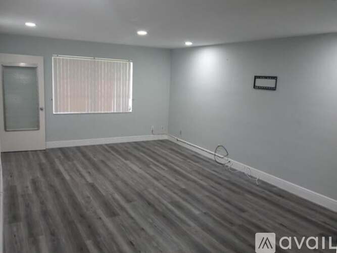 A room with grey walls and wooden flooring, with a window covered by blinds.