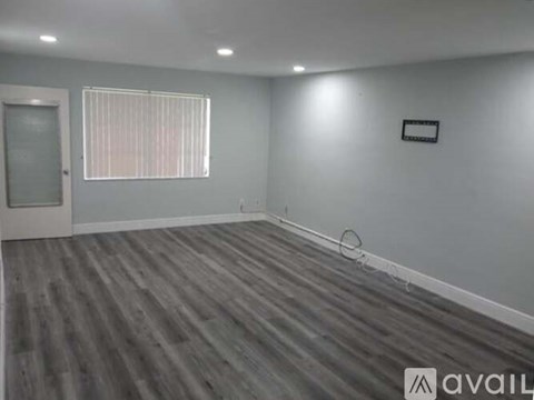 A room with grey walls and wooden flooring, with a window covered by blinds.