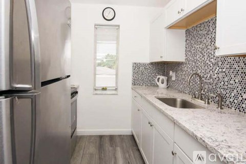 A kitchen with a stainless steel refrigerator and a sink with a tiled backsplash.