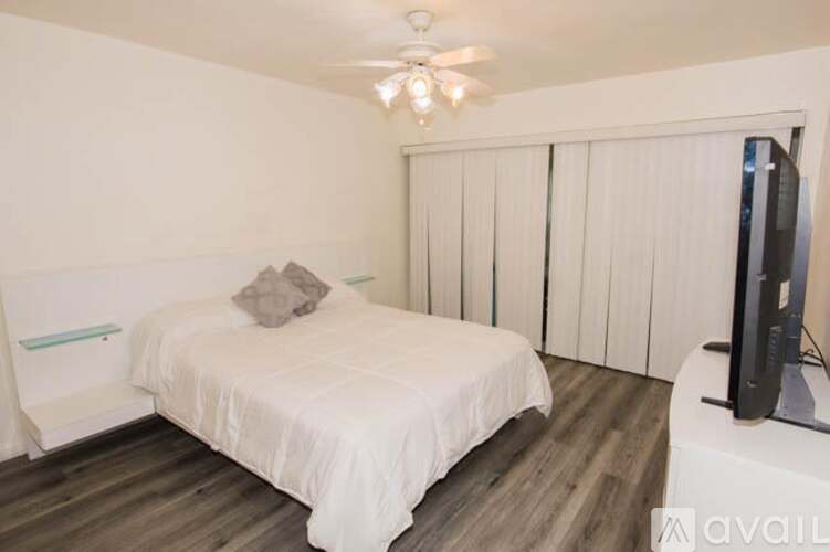 A bedroom with a bed, a television, and a window with blinds.