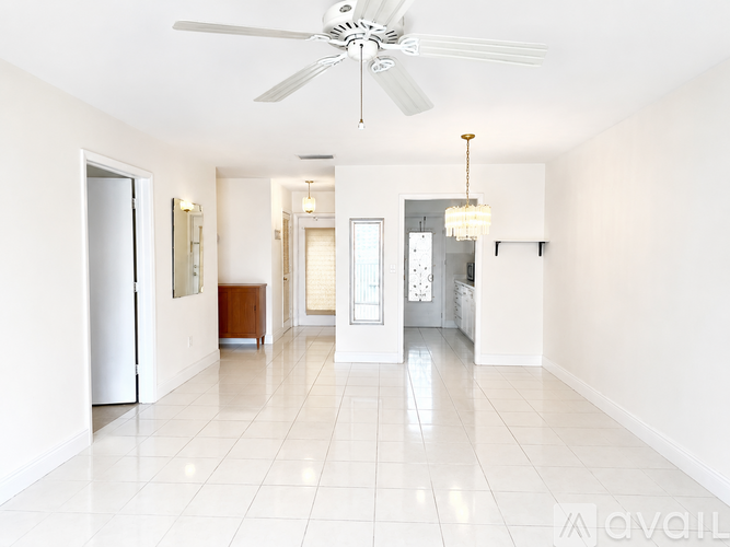 A spacious, white-walled room with a ceiling fan and a chandelier.