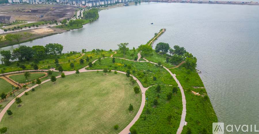 A large grassy park with a winding path and a body of water in the background.