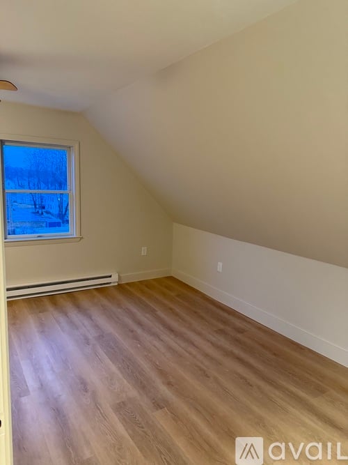 A room with wooden flooring and a window showing a snowy landscape outside.