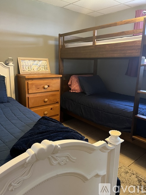 A bedroom with a white bed, a wooden dresser, and a bunk bed.