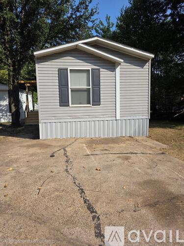A small house with a grey siding and a white window is situated in a driveway.