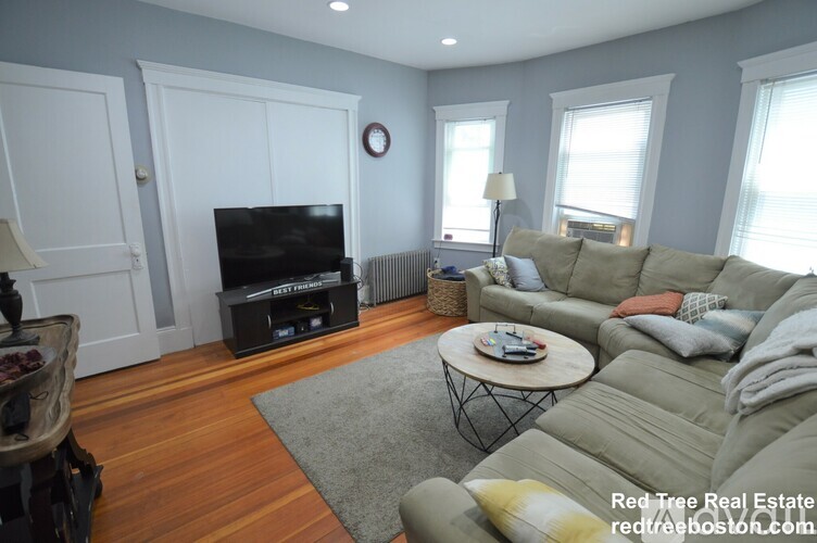 A living room with a grey couch, a flat screen TV, and a wooden floor.