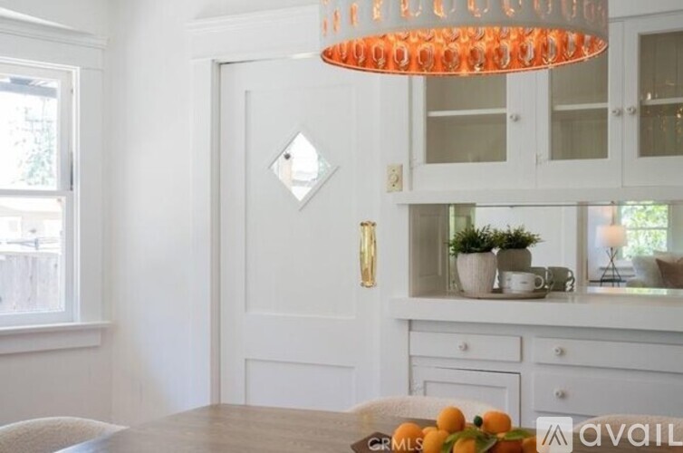 A kitchen with a white door, a chandelier, and a table with oranges on it.