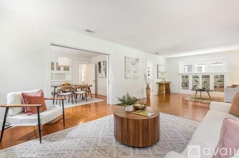 A living room with a white sofa, a wooden coffee table, and a dining table with chairs.