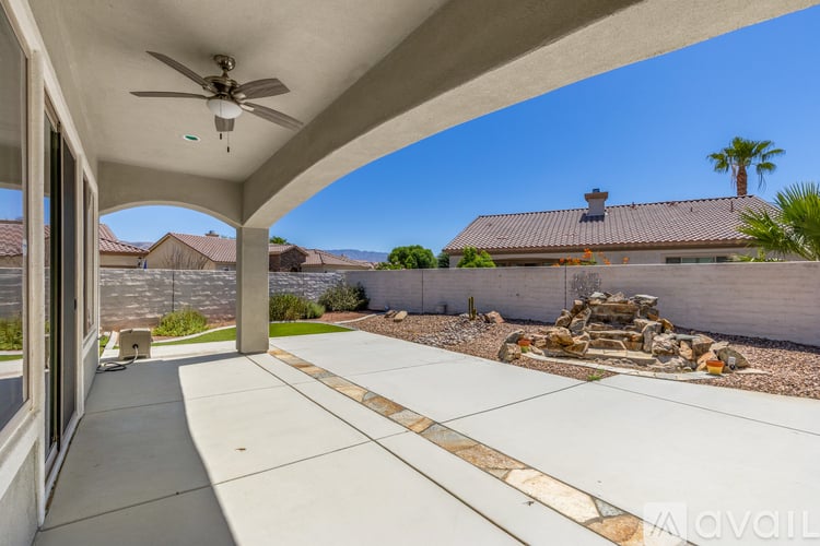 A patio with a ceiling fan and a view of a house and trees.
