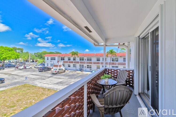 A balcony with a table and chairs overlooks a parking lot and buildings.