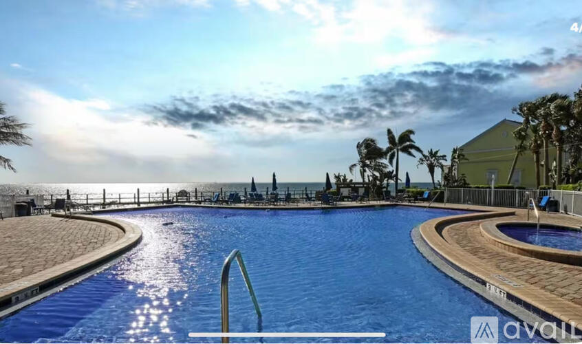 A large outdoor swimming pool with a sunny sky and palm trees in the background.