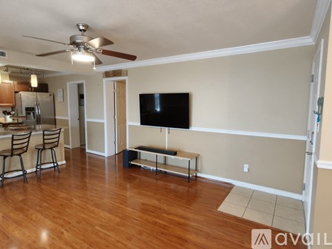 A living room with a television and a kitchen area in the background.