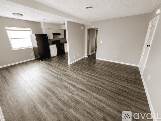 A spacious room with wood flooring and a kitchen area in the background.