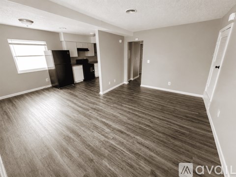 A spacious room with wood flooring and a kitchen area in the background.