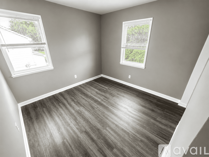 A room with wooden flooring and two windows.