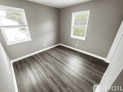 A room with wooden flooring and two windows.