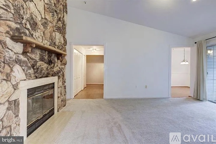 A spacious living room with a stone fireplace and carpeted floor.