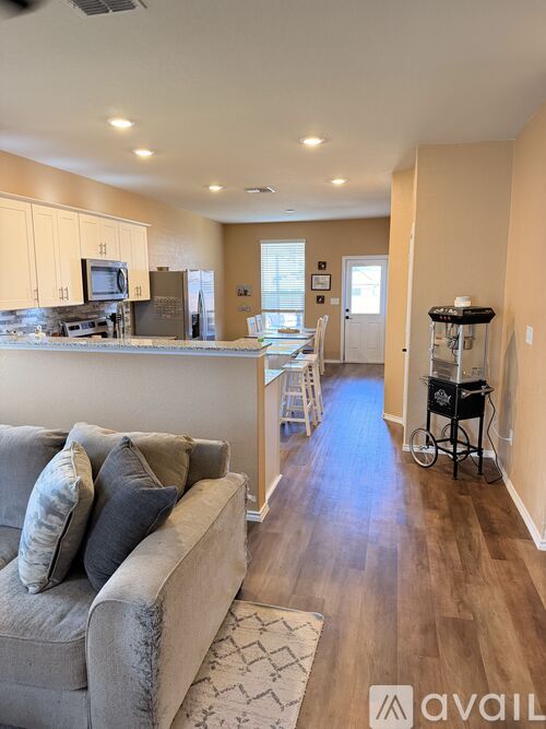 A living room with a grey couch and a kitchen area in the background.